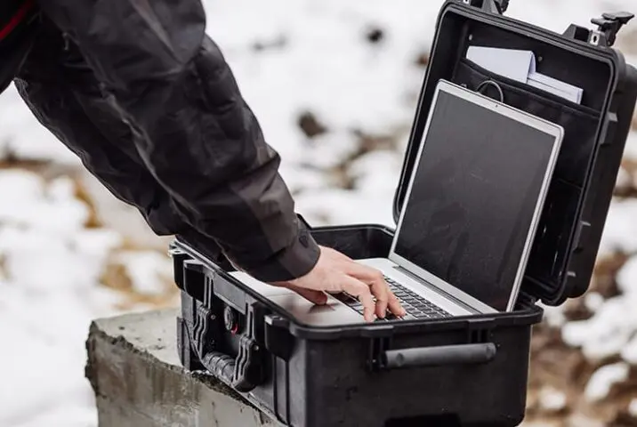 Person using a laptop outdoors in a rugged protective case on a snowy worksite.