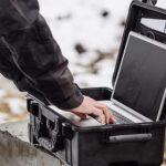 Person using a laptop outdoors in a rugged protective case on a snowy worksite.